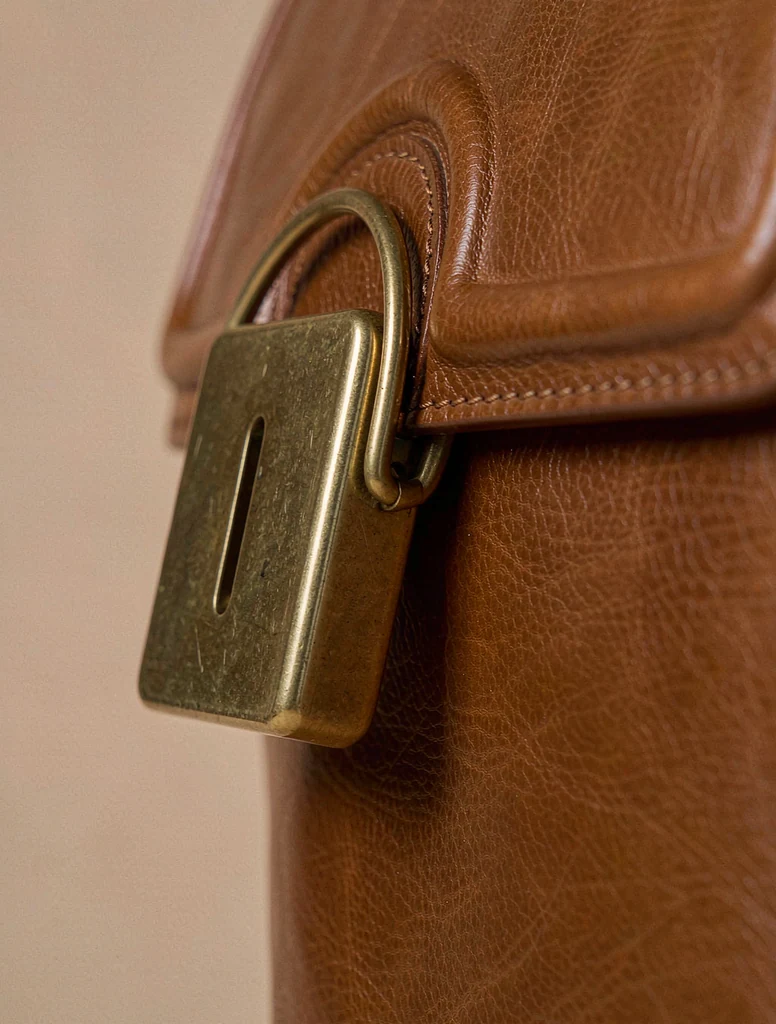 Close-up of a tan leather handbag with a solid brass clasp and hand stitching